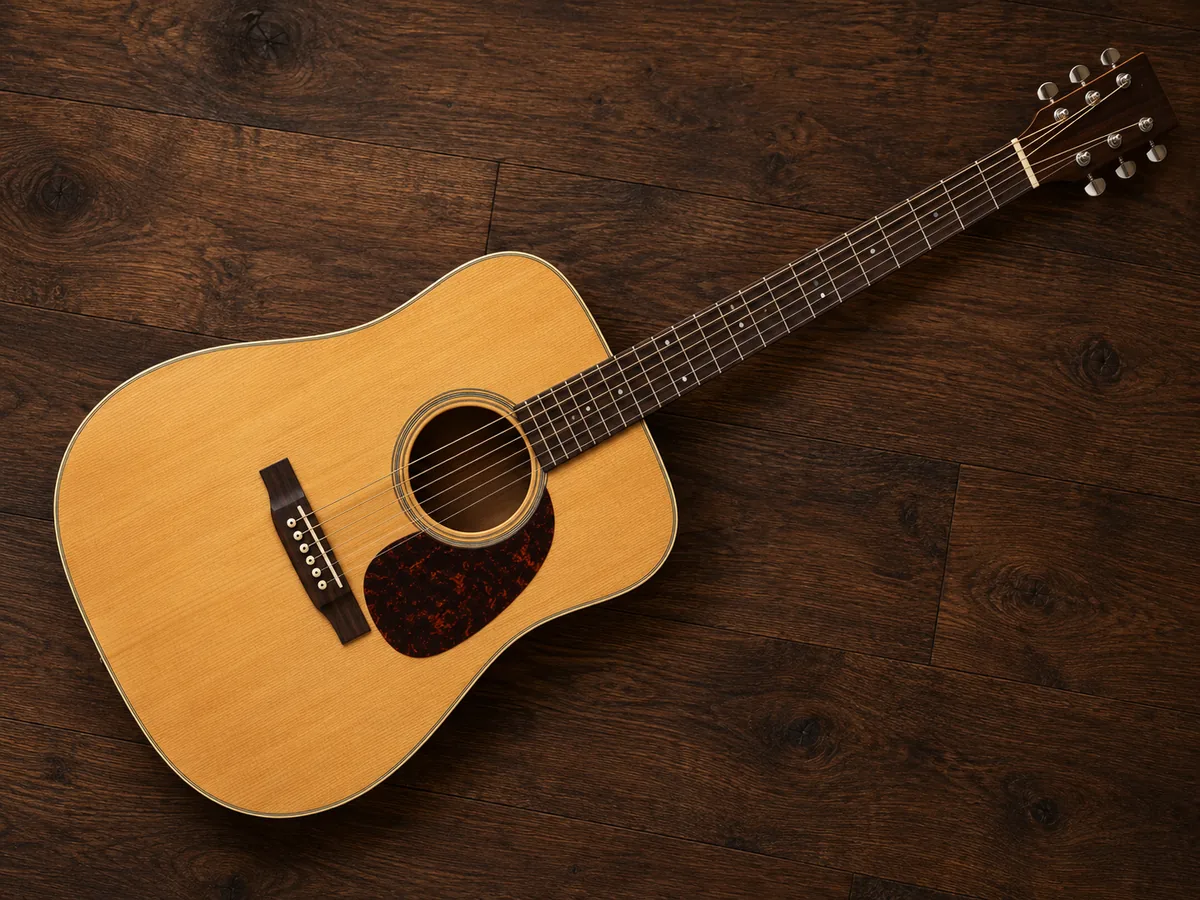 A symmetrical natural-finish acoustic guitar viewed directly from above on a walnut floor
